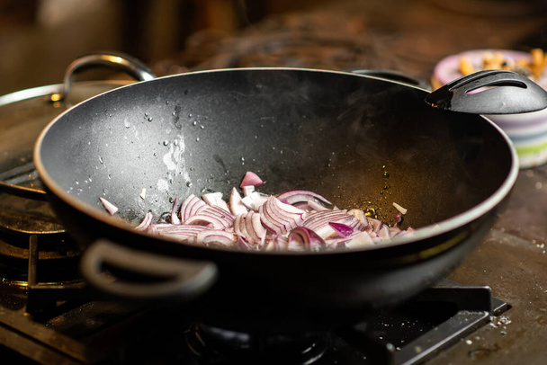 Fry the onion in a deep frying pan. Purple chopped onion is being prepared for cooking. - Foto, Bild