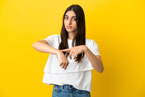 Young caucasian woman isolated on yellow background making the gesture of being late - Fotoğraf, Görsel