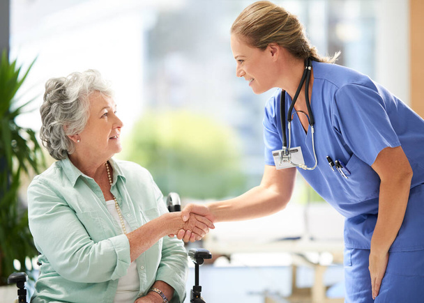 Handshake, nurse and elderly woman in wheelchair with medical results and surgery success news. Hospital, healthcare and clinic with women and nursing staff with care and support of senior person. - Foto, Imagen