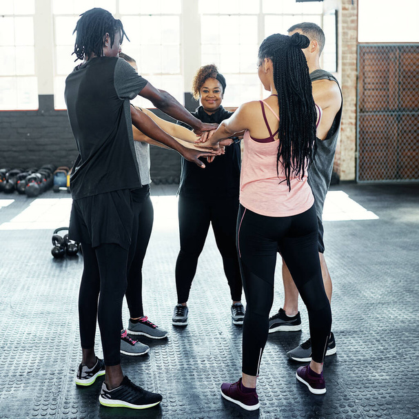 A fitneszről szól. egy vidám fiatal csoport, akik összebújnak, miközben az ember belenéz a kamerába edzés előtt egy edzőteremben. - Fotó, kép