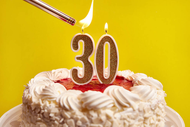 Uma vela na forma do número 30, presa em um bolo festivo, é acesa. Celebrar um aniversário ou um evento marcante. O clímax da celebração. - Foto, Imagem