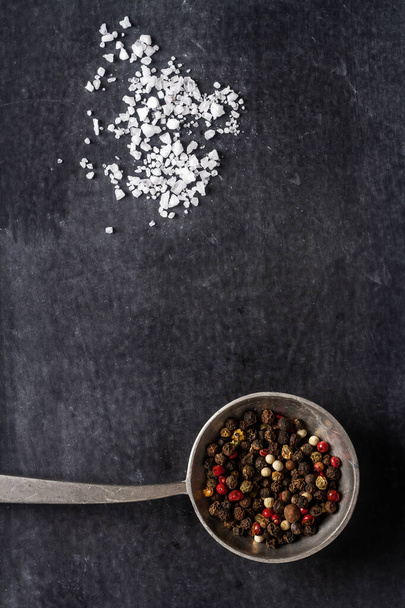 Big old spoon with peppercorn and salt pile on black background. Flat lay. Top view. Food concept. Dark mood food photography. - Zdjęcie, obraz