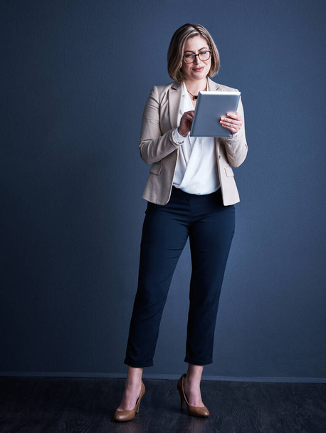She embodies everything it means to be corporate. Studio shot of an attractive young corporate businesswoman using a tablet against a dark background - Fotoğraf, Görsel