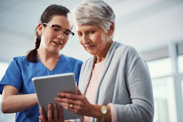 Todo lo que necesitas está aquí. una joven enfermera y su paciente mayor mirando una tableta en el hogar de ancianos - Foto, imagen