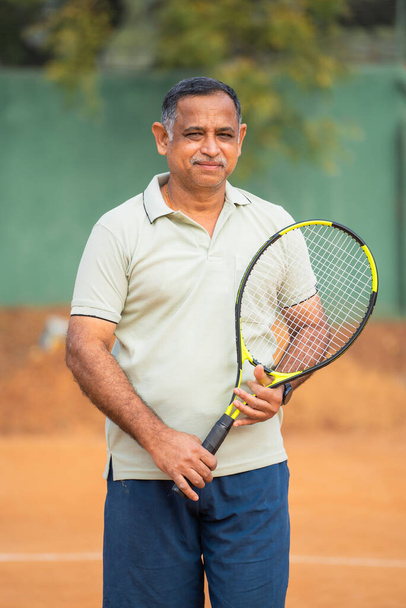 Heureux souriants hommes âgés indiens avec raquette et caméra à la recherche de balle au court de tennis concept de confiance, succès et détente. - Photo, image