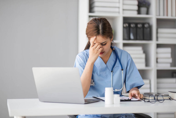Stressed young female doctor looking at laptop reading bad news online worried of mistake at workplace. Unhappy professional physician in tension feeling tired solving computer problem at work... - Photo, Image