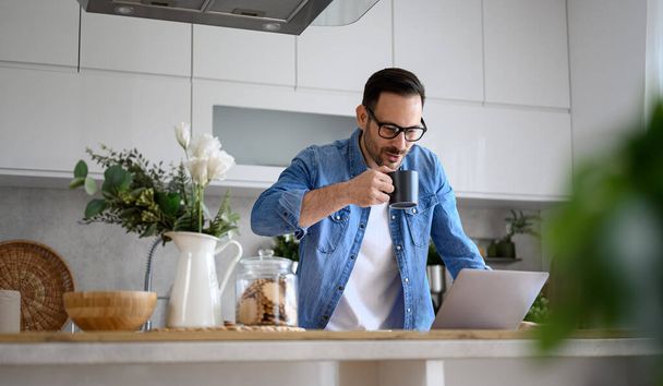 mężczyzna przedsiębiorca freelancer przy kawa i za pomocą laptopa na blacie kuchnia w domu biuro - Zdjęcie, obraz