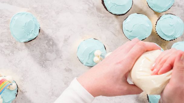 Plat gelegd. Stap voor stap. Versieren chocolade cupcakes met boterroom glazuur en regenboog snoep. - Foto, afbeelding