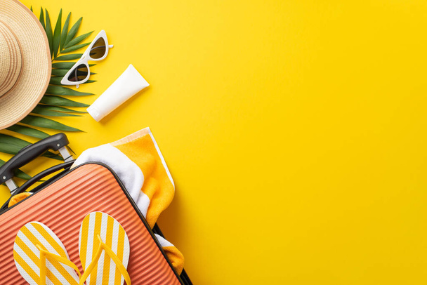 Sun-soaked dreams. Top view setup displaying a suitcase, beach essentials, glasses, sunhat, sunscreen, flip-flops, towel, palm leaf on vibrant yellow backdrop. Empty space provided for text or adverts - Photo, image