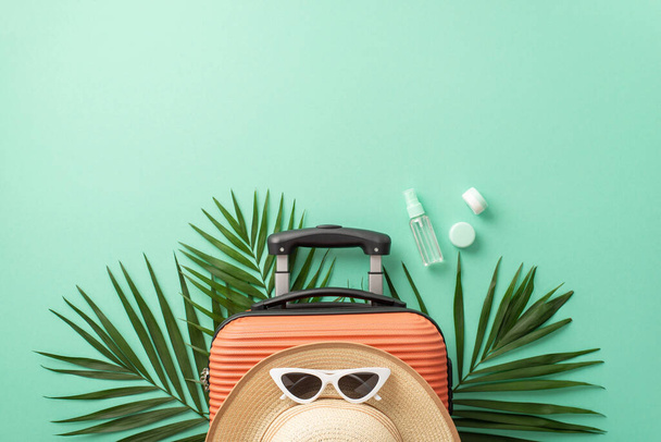 Un accattivante ambiente turchese pone le basi per una vista dall'alto di una valigia, attrezzatura da spiaggia, occhiali da sole, copricapo, bottiglie cosmetiche spf su foglie di palma. Ottimo per il marketing di viaggio - Foto, immagini