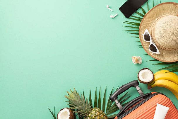 熱帯休暇の概念。サングラス、ヤシの葉、エキゾチックな果物、スマートフォン、ヘッドフォン付きのスーツケースと麦藁帽子のトップビューコピースペース付きの孤立したティール背景 - 写真・画像