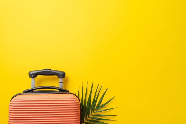 Φοβερή ιδέα για διακοπές. Πάνω άποψη φωτογραφία του πορτοκαλί βαλίτσα με φύλλο παλάμης από κάτω σε απομονωμένο φωτεινό κίτρινο φόντο με αντίγραφο-χώρο - Φωτογραφία, εικόνα