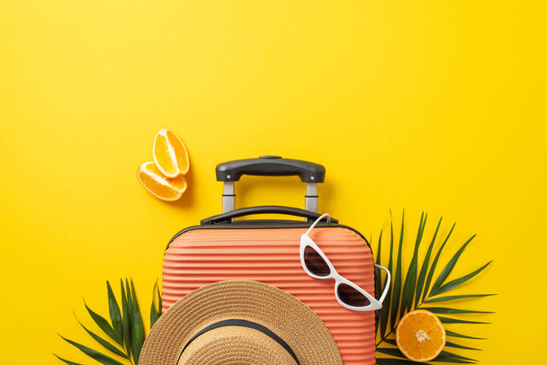Summer travel concept. Top view photo of orange suitcase with straw hat and sunglasses on it with palm leaves and oranges on isolated bright yellow background with copyspace - Foto, Imagem
