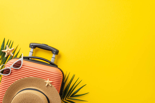 Dream vacation concept. Top view photo of orange suitcase with straw hat and sunglasses on it with palm leaves and starfish on isolated bright yellow background with copyspace - Фото, зображення