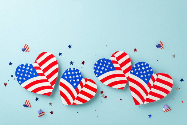 Patriotism on display for Independence Day. Top-down view perspective capturing symbolic decorations: hearts with American flag design, confetti against light blue background with space for text or ad - Фото, зображення