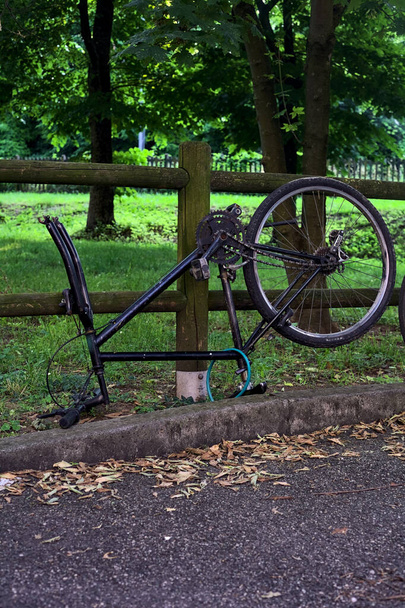 Broken bike leaning on a wooden fence in a park at sunset - Φωτογραφία, εικόνα