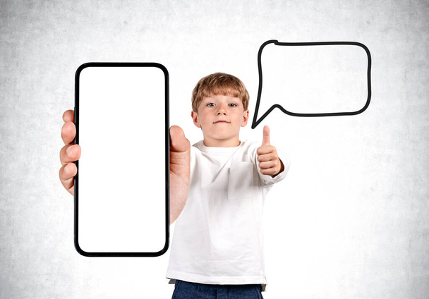 Young student wearing casual wear is holding smartphone case with copy space standing in front of white concrete wall in background. Speech bubble. Concept of mobile application and social media - Fotografie, Obrázek