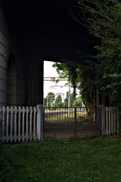 Railroad track in a park that passes under a concrete bridge in an italian town at sunset - Foto, afbeelding