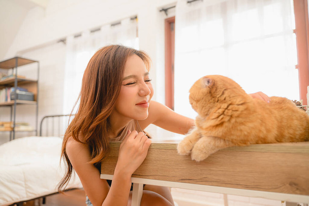 Μια γάτα με γυναίκα είναι στο σπίτι, μια νεαρή γυναίκα με ένα όμορφο γατάκι στην κρεβατοκάμαρά της. Είναι χαρούμενη και χαρούμενη, απολαμβάνοντας την παρέα του κατοικίδιου της. - Φωτογραφία, εικόνα