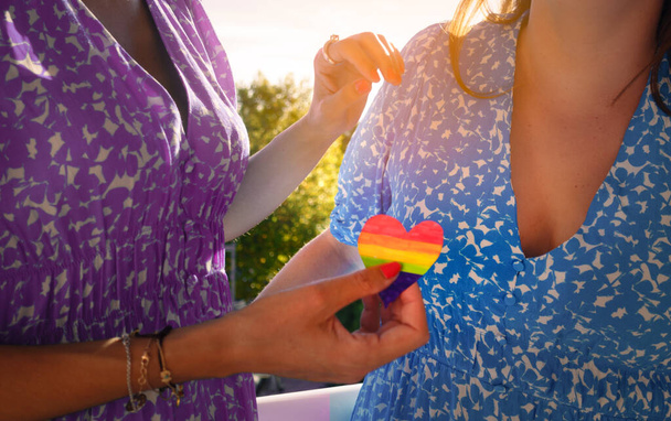 Ανώνυμο ζευγάρι λεσβιών που μοιράζονται μια καρδιά με τα χρώματα του ουράνιου τόξου. ΛΟΑΤ λεσβιακά ζευγάρια αγαπούν τις στιγμές και την έννοια της ευτυχίας - Φωτογραφία, εικόνα