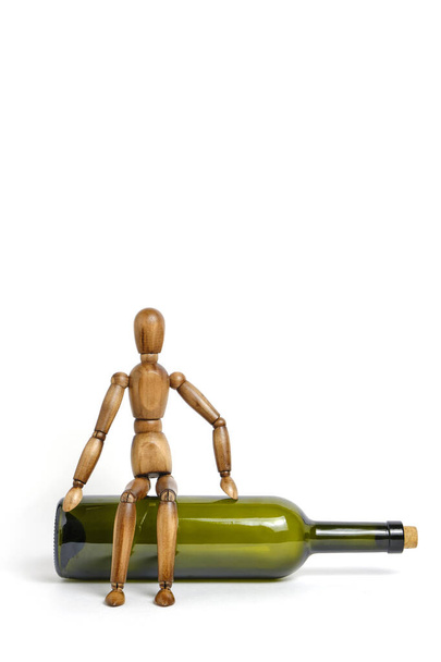Wooden mannequin sits on an empty bottle of wine.Concept of alcohol abuse and dependence - Photo, Image