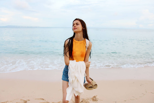 Une jeune femme après avoir nagé dans l'océan avec un sac à dos en vêtements humides se promène le long de la plage, vacances d'été sur une île au bord de l'océan à Bali coucher de soleil. Photo de haute qualité - Photo, image