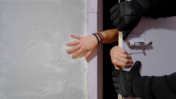   dívčí ruce, mezi zdí a vězeňskými dveřmi, které se muž v rukavicích snaží zavřít.koncept: žena se snaží dostat z vězení. vězení. žena v zajetí                                        - Fotografie, Obrázek