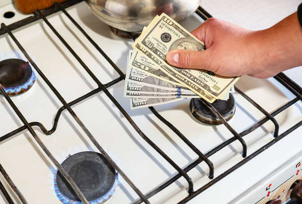 Payment of utility services. Dollar bills are held in their hands near a burning gas burner. The concept of increasing the cost of natural gas supply and payment - 写真・画像