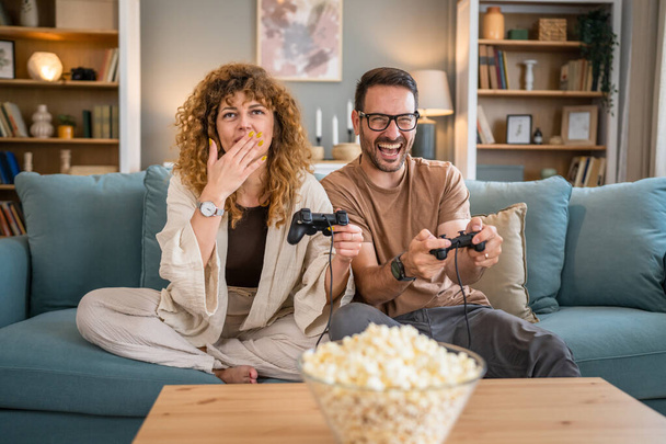 Adult couple man and woman caucasian husband and wife or boyfriend and girlfriend play console video games at home hold joystick controller have fun leisure joy and bonding concept copy space - Photo, Image