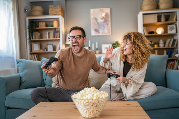 Adult couple man and woman caucasian husband and wife or boyfriend and girlfriend play console video games at home hold joystick controller have fun leisure joy and bonding concept copy space - Fotó, kép