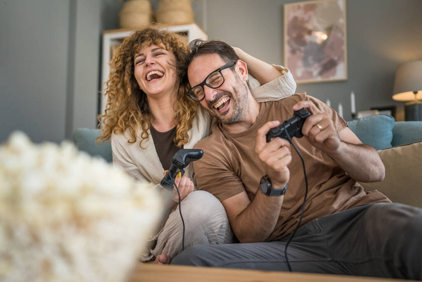 Adult couple man and woman caucasian husband and wife or boyfriend and girlfriend play console video games at home hold joystick controller have fun leisure joy and bonding concept copy space - Photo, image