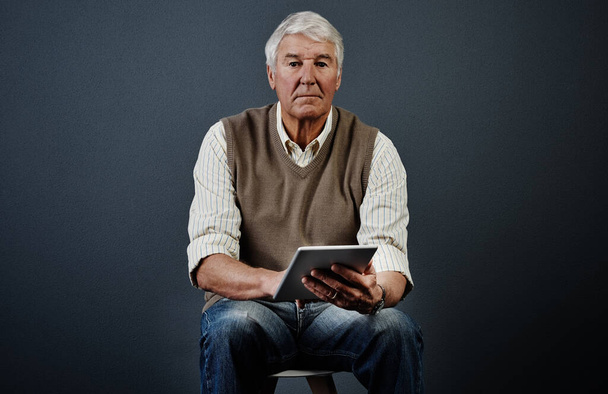 Im still learning a thing or two. Studio portrait of a handsome mature man using a tablet while sitting on a wooden stool against a dark background - Fotó, kép