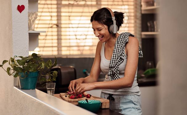 Music headphones, morning and woman cooking breakfast of healthy strawberry food at home. Kitchen, headphone and happy female person making snack with fruits while listening to audio, sound and radio. - Foto, Bild