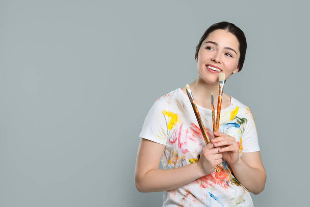 Woman with paintbrushes on grey background, space for text. Young artist - Photo, image