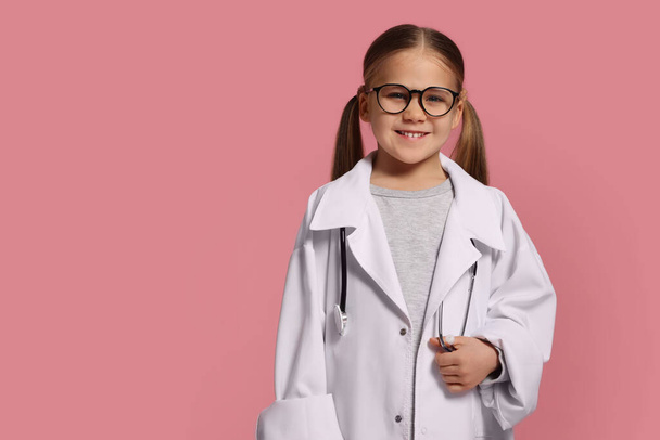 Little girl in medical uniform with stethoscope on pink background. Space for text - Фото, зображення