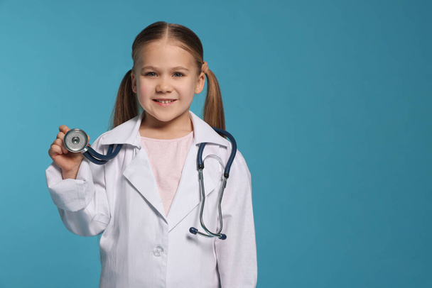 Little girl in medical uniform with stethoscope on light blue background. Space for text - Photo, Image