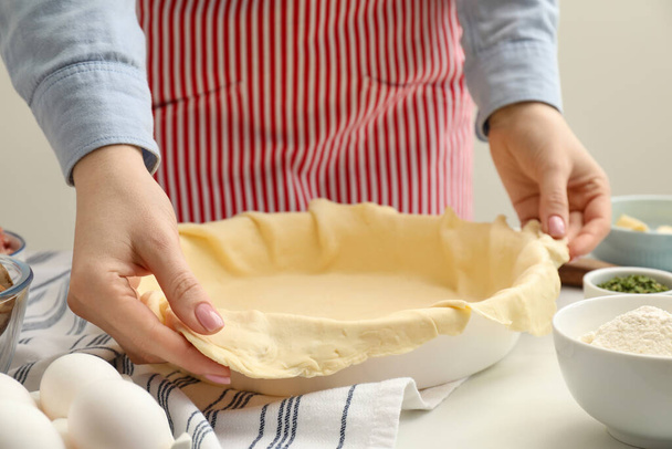 Женщина кладет тесто для мясного пирога в выпечку блюдо за белым столом, крупным планом - Фото, изображение