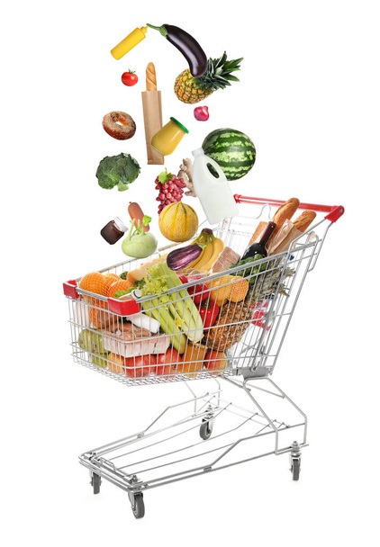 Market assortment. Different products falling into shopping cart on white background - Foto, Imagen