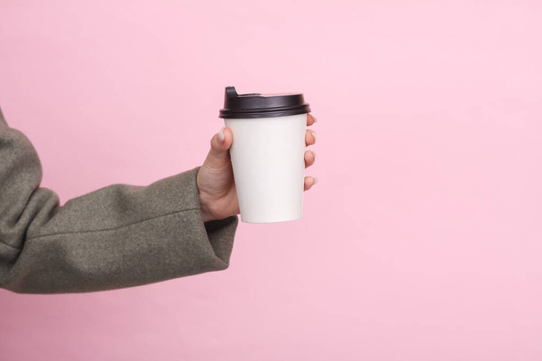 Woman's hand in a woolen coat holds a white cardboard coffee cup mockup on a pink background. - Foto, immagini