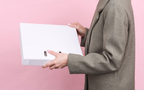 Επιχειρηματίας γυναίκα σε μάλλινο παλτό κρατώντας λευκό φάκελο mockup σε ροζ φόντο - Φωτογραφία, εικόνα