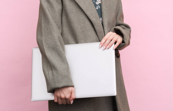 Woman in wool coat holding closed laptop on pink background - Photo, Image
