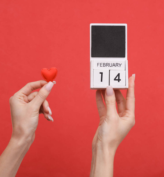 Női kéz kezében fa naptár dátum február 14 és a szív a piros háttér. Valentin-nap - Fotó, kép