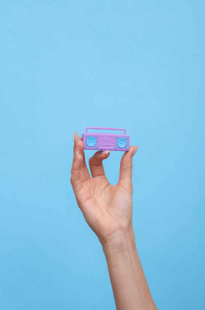 Female hand holding a miniature of retro boombox tape recorder on blue background. - Photo, Image