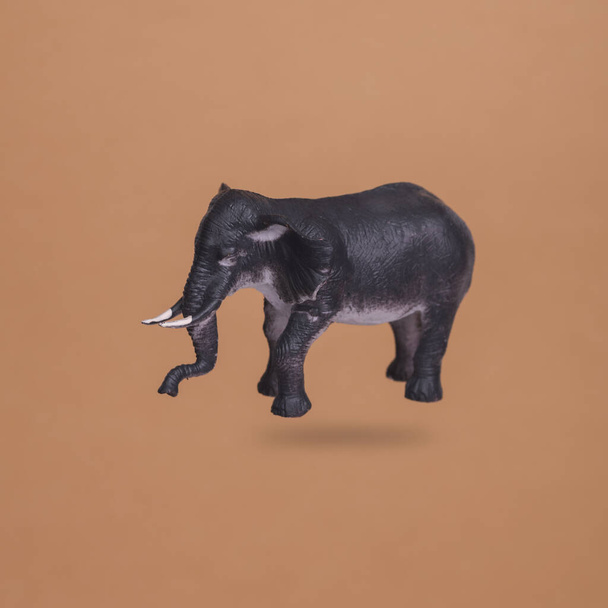 Пластиковая миниатюра слона левитирует на коричневом фоне с тенью - Фото, изображение
