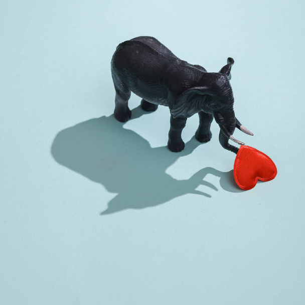 Plastic elephant with heart on blue background. Love concept, valentine's day, february 14th celebration, creative layout - 写真・画像