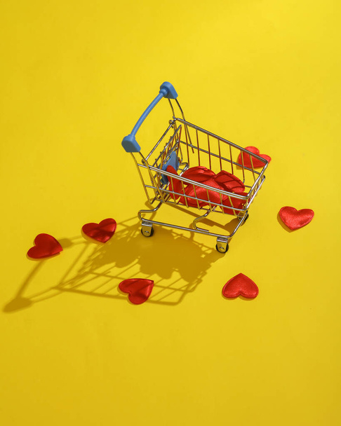 Shopping trolley with hearts on yellow background. Love concept, valentine's day, february 14th celebration, holiday shopping, creative layout - Photo, Image