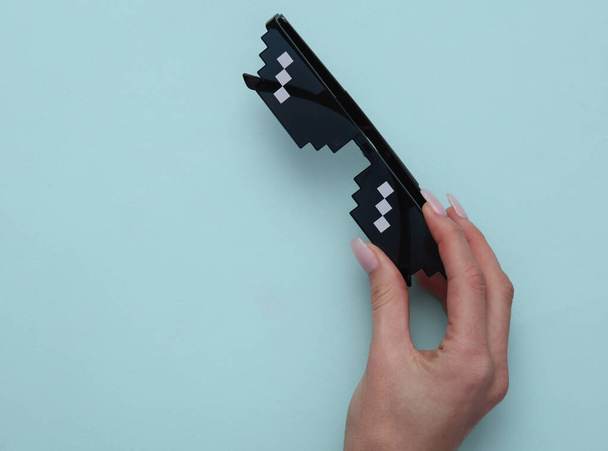 Рука женщины держит пиксельные очки на синем фоне - Фото, изображение
