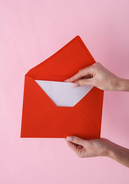 Les mains féminines tiennent une enveloppe rouge avec une lettre blanche vide sur fond rose - Photo, image