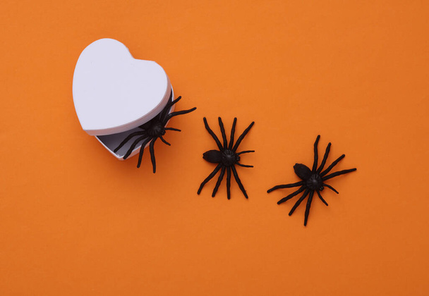 Декоративні павуки виповзають з коробки у формі серця на оранжевому тлі. Концепція Хелловін - Фото, зображення
