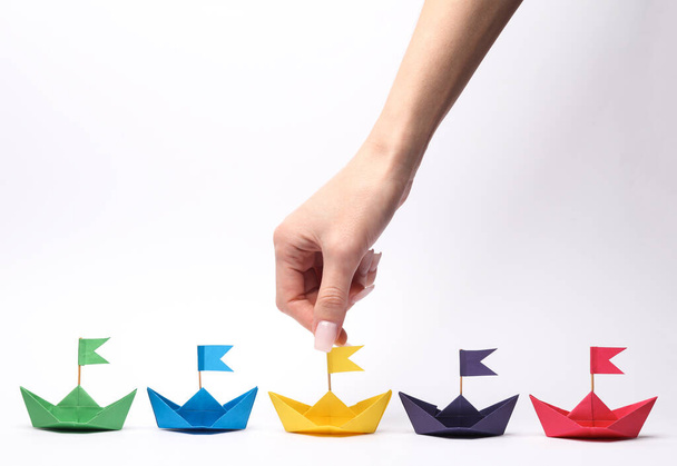 Hand chooses paper boats with flags on white background. Business, leadership concept - Photo, Image